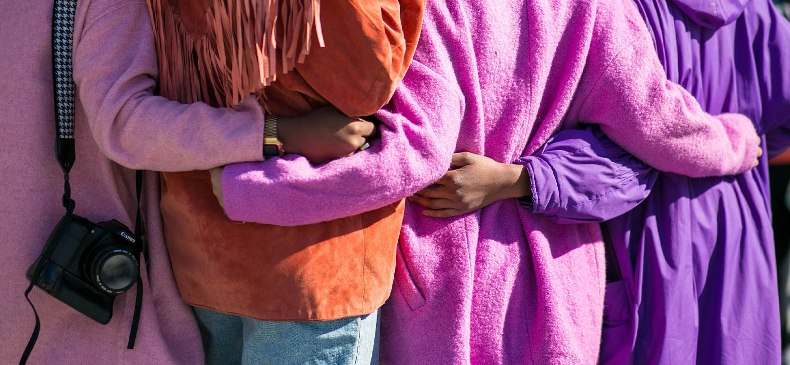 Mid-shot of four people wearing colourful fluffy coats holding each other's backs
