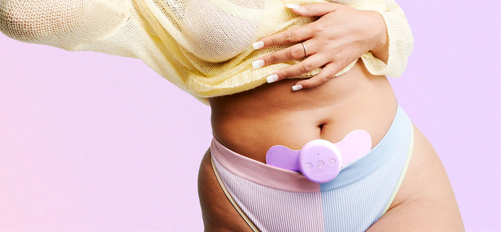 Mid shot of person's midrift wearing blue and purple underwear and cropped yellow jumper with VUSH Aura purple pain relief device on lower stomach against purple/pink gradient background